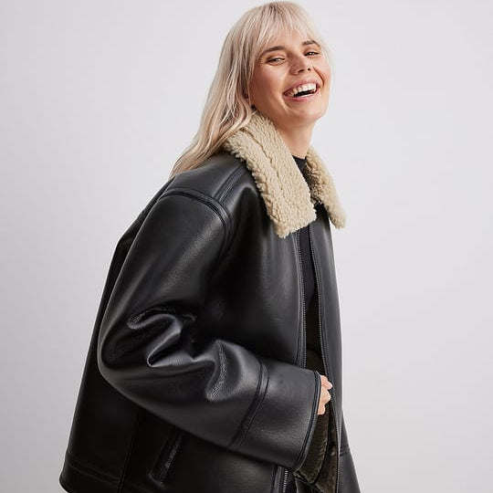 Woman wearing black shearling aviator jacket over sweater, styled with jeans